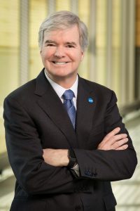 Mark Emmert standing, smiling with arms crossed on his chest