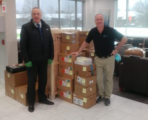 Doug Smith standing to the left of donated packages, Dr. Todd Shatkin standing to the right of the donation