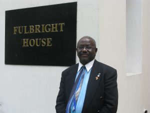 Dr. Joseph Sankoh in a suit standing in front of the Fullbright House sign in India