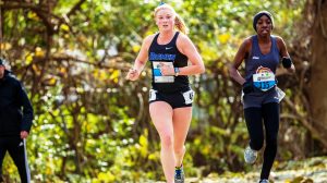 Female cross country athlete running in woods with competitor behind her