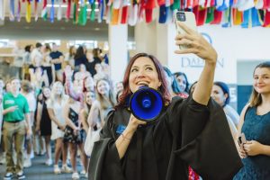 Kerry Spicer in Commencement robes taking a selfie with students