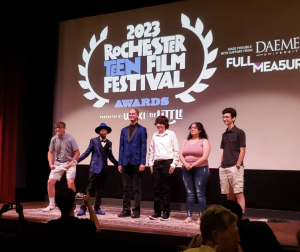 Students posing on stage with 2023 film festival on the screen behind them