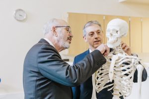 Scott Bieler and Dr. Greg Ford in the physical therapy lab looking at a model skeleton.