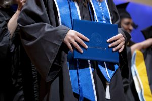 Student holding diploma holder while getting hooded at commencement