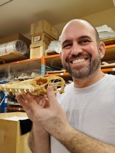 Man holding skeleton of a Komodo dragon in a storage room with shelves behind him