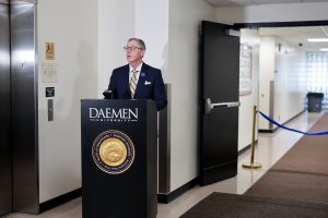 Image of Dr. Ford, dressed in suit and tie in front of the Daemen podium speaking to an audience