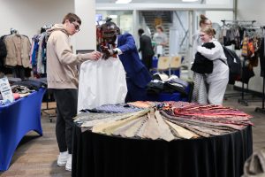 A table filled with neck ties with a student and staff holding and looking at a white dress shirt 