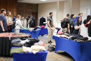 A room with several tables and clothing racks with business attire on display. Students browsing apparel.