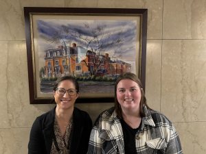 Two female Daemen students stand in front of a picture at the Buffalo Club