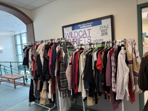 clothing rack filled with a variety of hanging clothing in front of Wildcat Thrifts sign