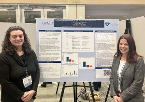 Two women with long brown hair standing in front of a research poster on an easel