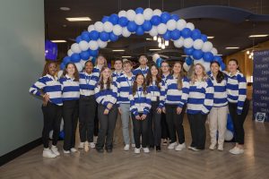 Group of students wearing blue and white striped long sleeved shirts in front of blue and white balloon arch