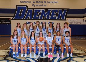 Image of 15 female basketball players in light gray Daemen uniforms in the gymnasium. Eight women are standing and seven women are sitting. 