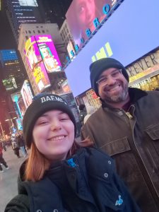 Female and male wearing winter hats in New York City with bright lights on buildings in Times Square in the backdrop