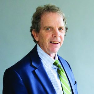 Middle aged male with salt and pepper hair wearing a white shirt with light plaid, a kelly green tie and a royal blue blazer