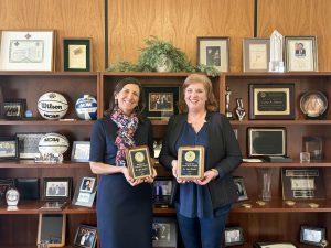 Two women standing in front of a bookcase holding awards in their hands