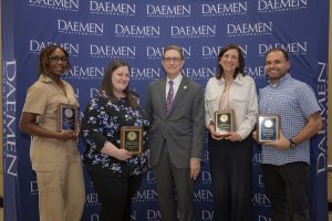 Five people standing in front of a blue Daemen 