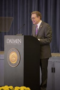 Middle-aged male dressed in a suit and tie standing behind a podium giving a speech