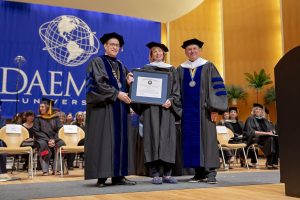 Two men and a woman wearing cap and gowns holding a framed degree certificate