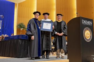 Three men wearing caps and gowns holding a framed diploma certificate