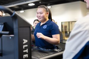 Female dressed in a blue shirt with her hair pulled back in a ponytail walking in the Alter-G physical therapy treadmill