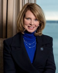 Woman with shoulder length blonde hair wearing a royal blue turtleneck and navy blazer