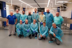 Thirteen men and women wearing medical gowns inside a lab