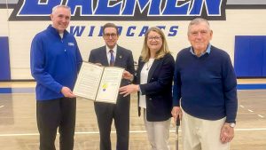 Three men and one woman standing in a gymnasium holding a certificate of recognition.