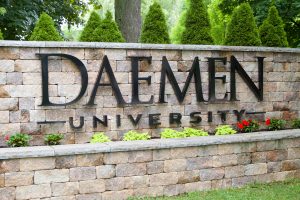 Stone wall with Daemen University sign on it and flowers planted underneath.