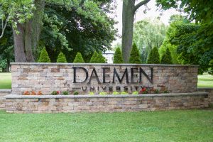 Stone wall with the words Daemen University on it with grass and trees around it