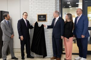 Two men dressed in suits unveiling a plaque on the wall with two men and a woman watching