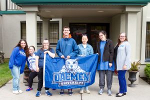 Group of students holding a Daemen flag standing in front of a building