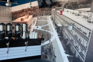 Wall with image of the Daemen quad (buildings, grass, sidewalks and fountain) on it. Bar with coffee