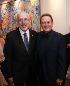 Two men dressed in suits standing together in front of a colorful painting