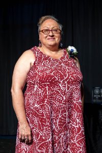 Woman wearing a red dress with white accents and a corsage standing in front of a dark curtain.