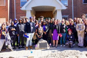 Group of men and women standing together behind a memorial stone with purple pinwheels on both sides of it
