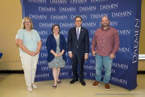 Two men and two women dressed nicely standing in front of a blue Daemen backdrop