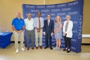 Four men and two women dressed nicely standing in front of a blue Daemen backdrop