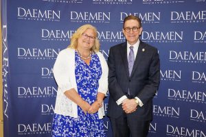 Man and woman dressed nicely standing in front of a blue Daemen backdrop