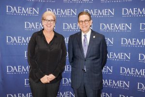 Man and woman dressed nicely standing in front of a blue Daemen backdrop
