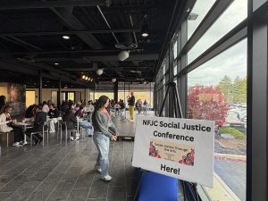 A room filled with tables and chairs with people sitting at them and a white sign with black text on an easel