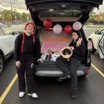 Two women standing in front of a car trunk that's decorated as Dunkin' Donuts.
