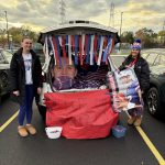 Two young women wearing long pants and jackets standing by a trunk of a car that's Buffalo Bills themed