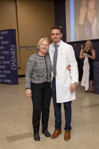 Male graduate nursing student wearing white coat standing with a female