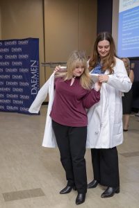Female graduate nursing student wearing white coat that another female is putting on her