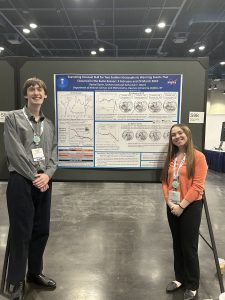 Two college students standing in front of a scientific poster with images and text on it
