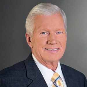 Headshot of man with gray hair, wearing a dark suit, white shirt and yellow striped tie.