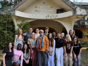16 people standing in front of the entrance to a building with silver metal text on it
