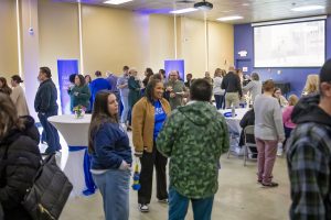 Large room with tall round tables filled with a group of people standing 