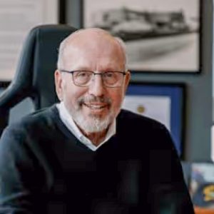 Man with gray hair and a beard wearing glasses and a white dress shirt underneath a dark sweater